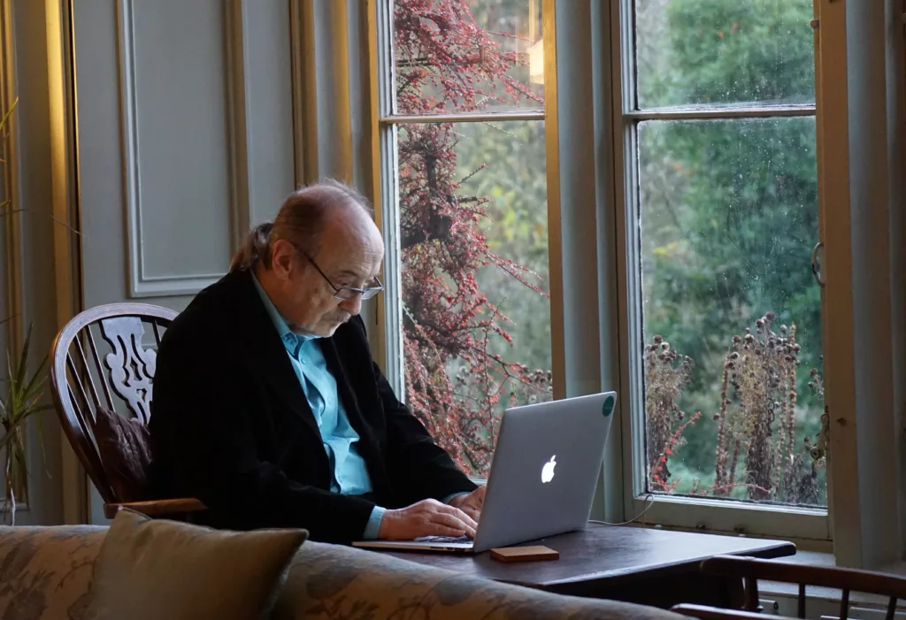 older man sitting at table typing on laptop computer