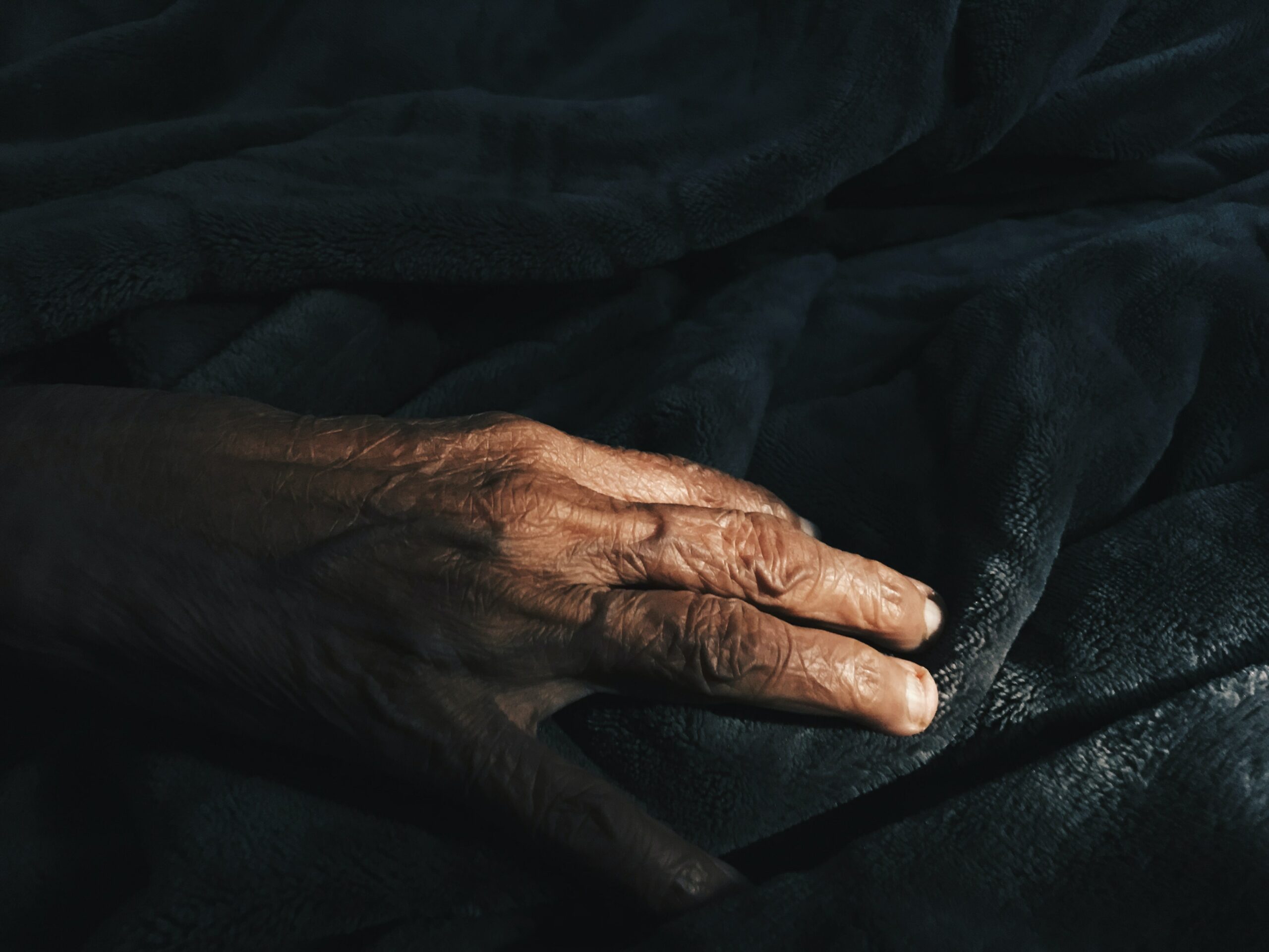 hand of older person resting on dark blanket
